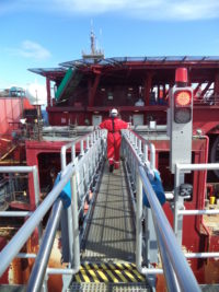 Man in red helicopter gear walks long a steel bridge 