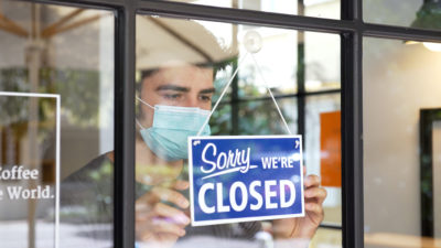 Man wearing mask hangs a closed sign in a window