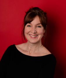 Jo Lochhead smiles at the camera in front of a red background