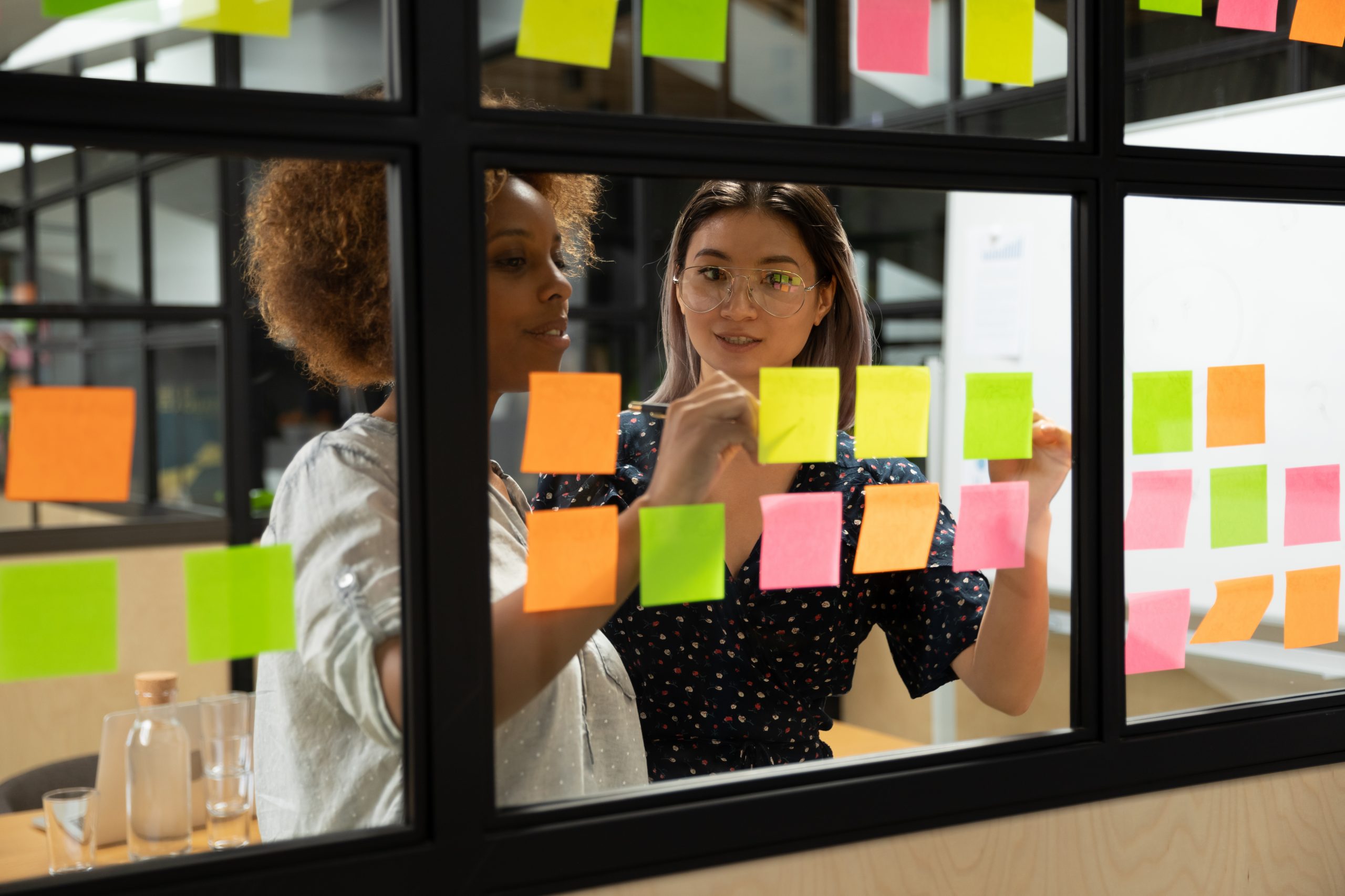 Two women work together with post-it notes on a board
